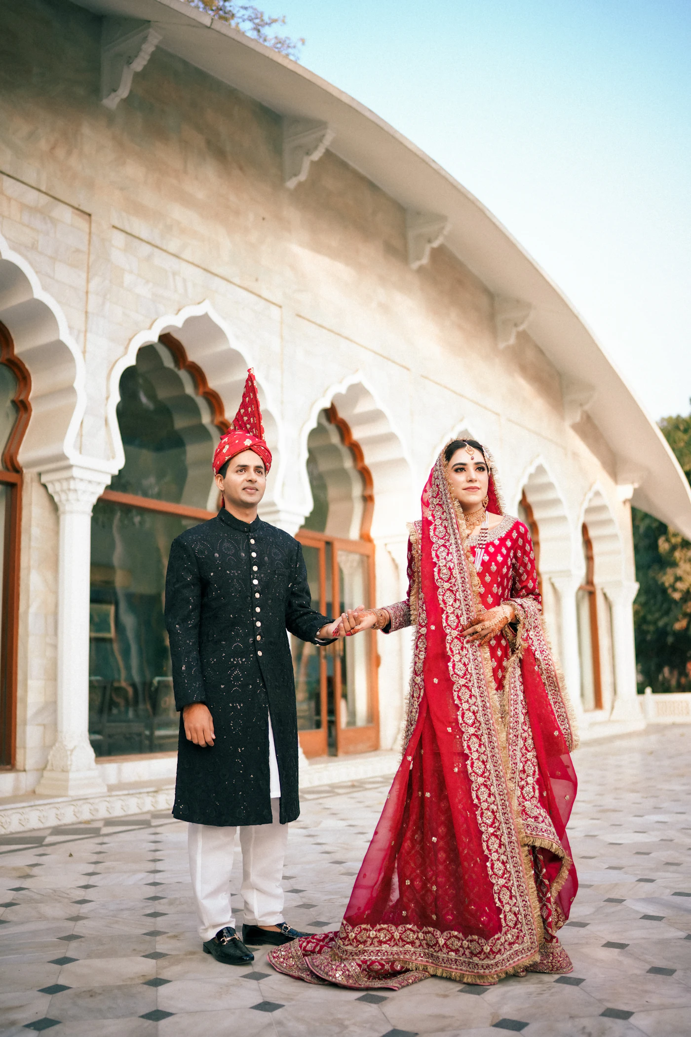 Bride and groom in red and black holding hands under white arches.