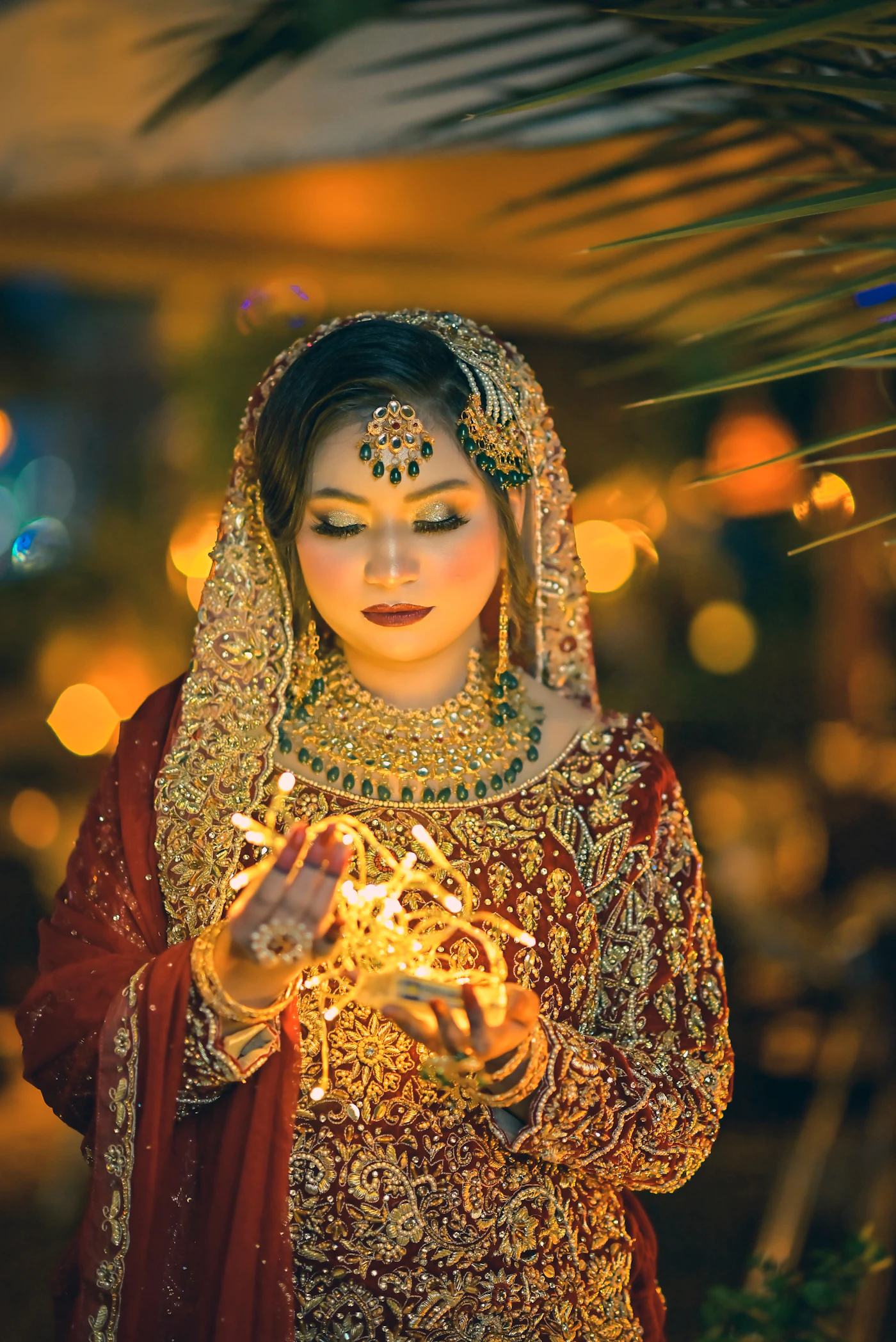 A bride in red and gold lit by a candle she is holding.