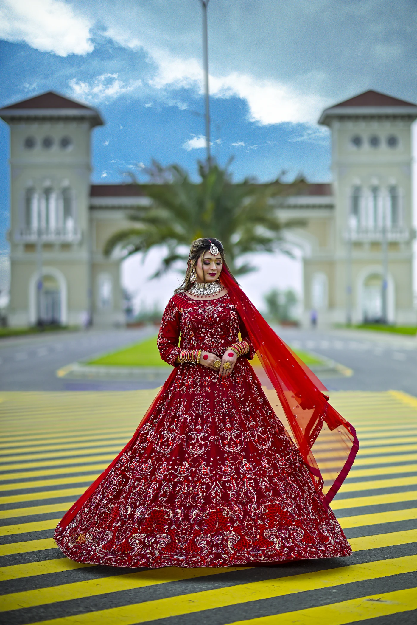 A bride in a red lehenga on a lawn in front of a white palace.