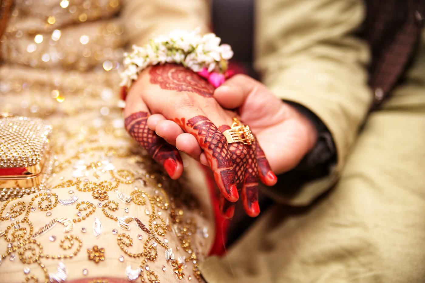 A bride’s hennaed hand in the groom’s hand, a gold ring on her finger.