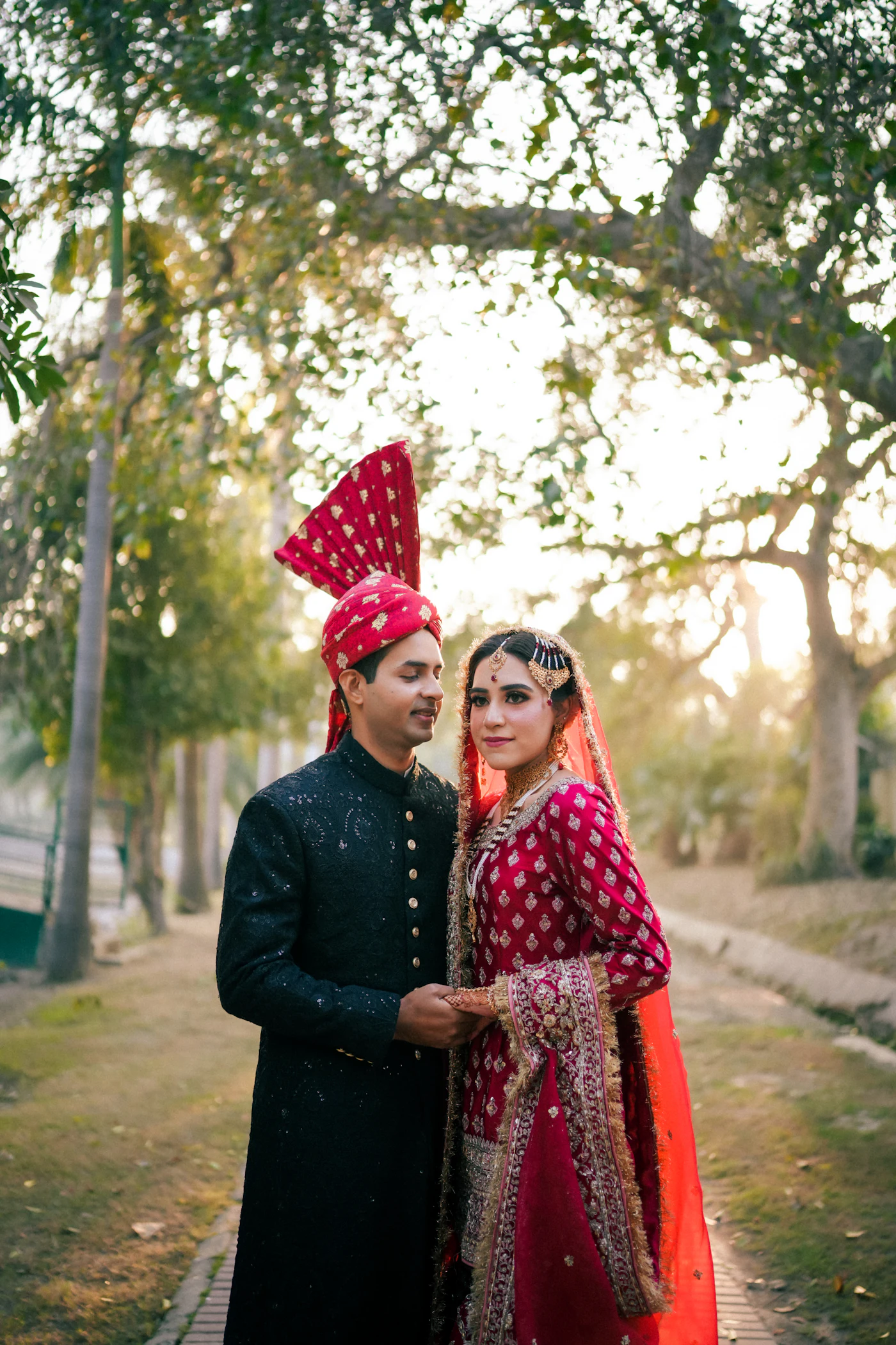 Bride and groom walking together on a tree lined path at sunset.